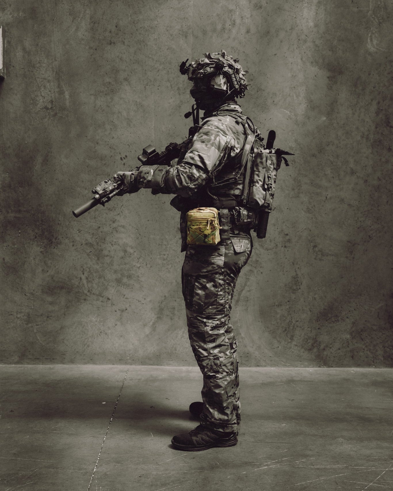 Person in military gear with a rifle against a gray background