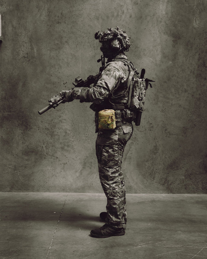 Person in military gear with a rifle against a gray background